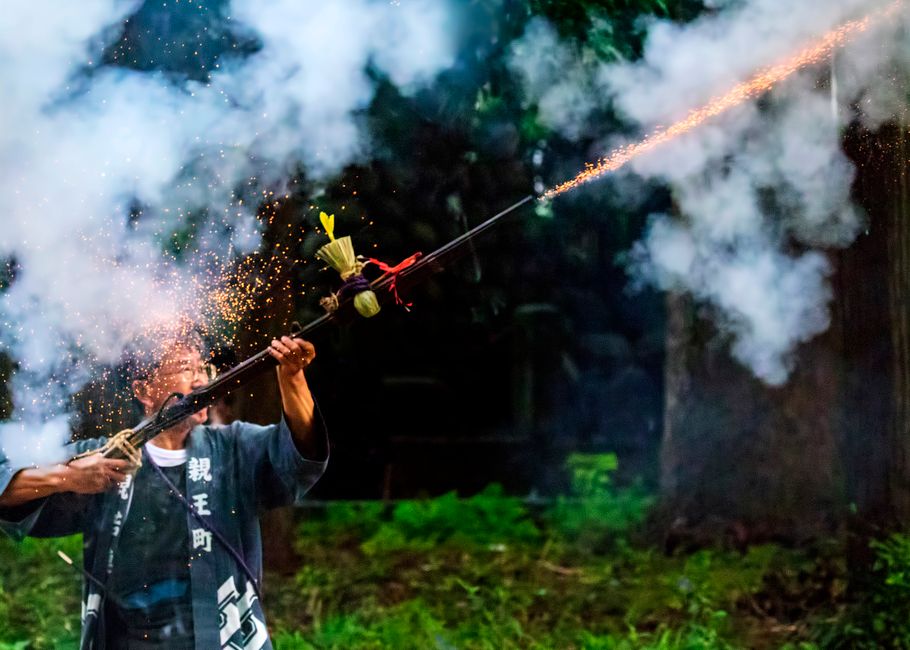 An Asian man in traditional attire launches fireworks in a vibrant outdoor ceremony.
